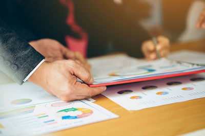 Cropped hands of businessman with colleague holding chart at office