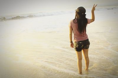 Rear view of young woman showing peace sign at beach