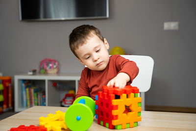 A cute attentive little toddler boy of two years old sits at a children's table and plays