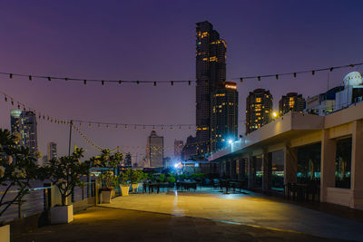 Illuminated street amidst buildings against sky at night
