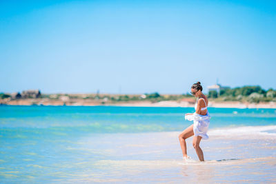 Full length of young woman at beach against clear sky