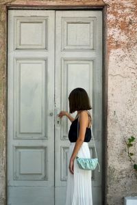 Side view of woman standing against closed door of building