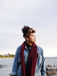 Thoughtful young woman standing at beach against sky