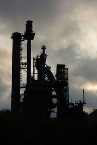 Low angle view of silhouette factory against sky at sunset