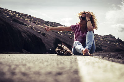 Woman sitting on road against sky