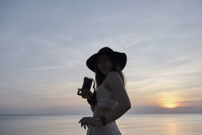 Side view of woman standing against sea during sunset