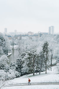 Person on snow covered buildings in city against sky