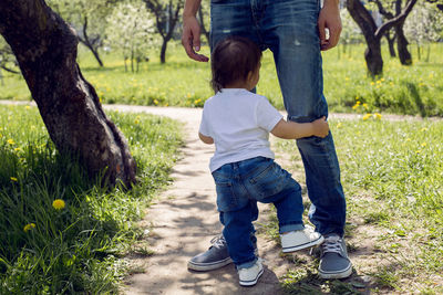 Baby boy standing at his father's feet in a green garden in the village