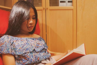 Close-up of young woman reading book while sitting at home