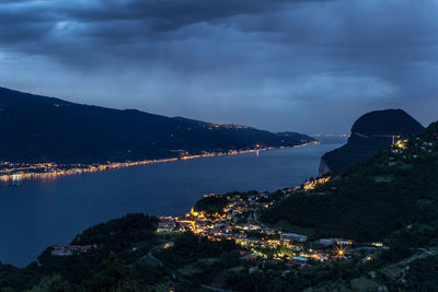 Aerial view of illuminated city by sea against sky