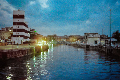 Illuminated city by water against sky at night