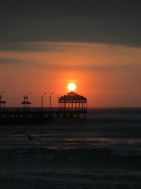 Silhouette built structure on beach against orange sky