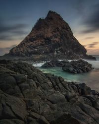 Rock formation on shore against sky during sunset