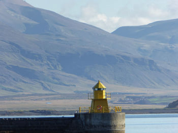 Lighthouse amidst buildings and mountains against sky