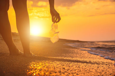 Low section of woman walking on beach during sunset