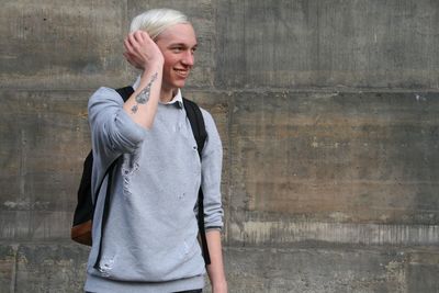 Smiling man looking away while standing by wall