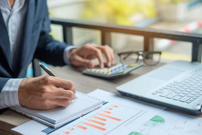 Midsection of businessman writing in diary at desk in office