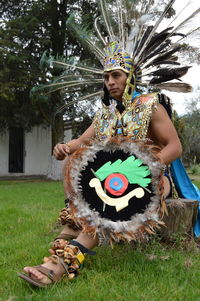 Man wearing tribal costume sitting on tree stump