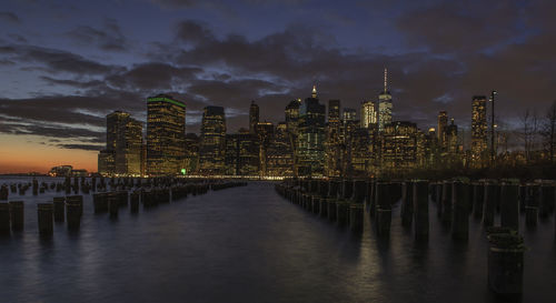 Illuminated buildings by river against sky at night