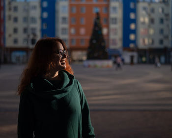 Portrait of young woman looking away while standing in city