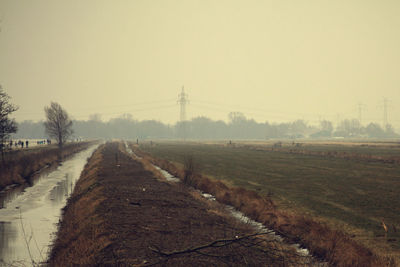 Road amidst field against sky during foggy weather