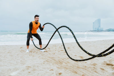 Male athlete exercising with rope at beach