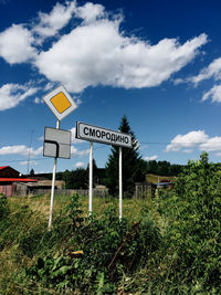 Road sign on field against sky