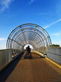 Rear view of man riding bicycle on footbridge