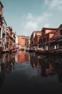 Boats moored on canal amidst buildings against sky