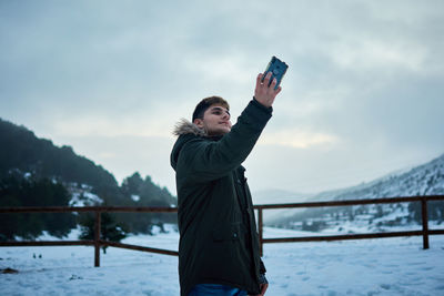 A young man takes a selfie with his mobile phone on a snowy day