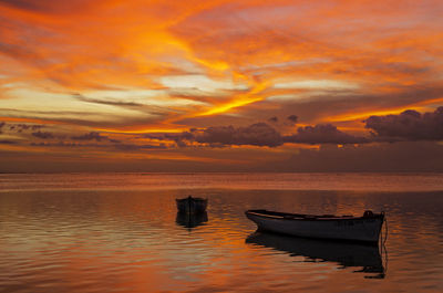 Boat moored in sea against orange sky