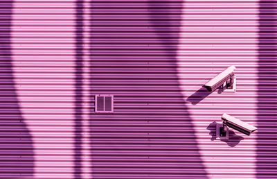 Low angle view of security cameras on pink wall