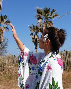 Midsection of woman against trees and blue sky