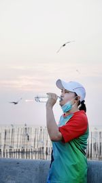 Side view of woman drinking water against sky