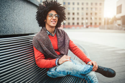 Smiling young man with afro hairstyle sitting in city