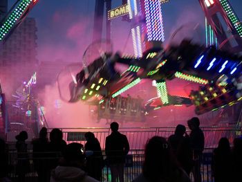 People looking at illuminated amusement park ride during night