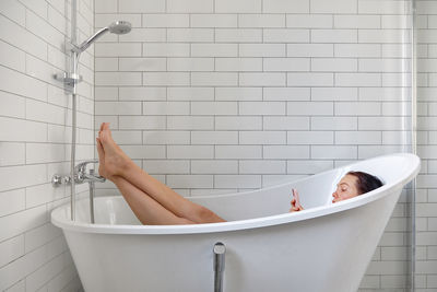 Full length of woman using mobile phone sitting in bathtub