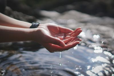 Cropped image of woman with wet cupped hands over lake