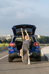 Full length of woman sitting in car trunk