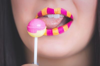 Cropped image of woman with yellow and pink lipstick licking lollipop