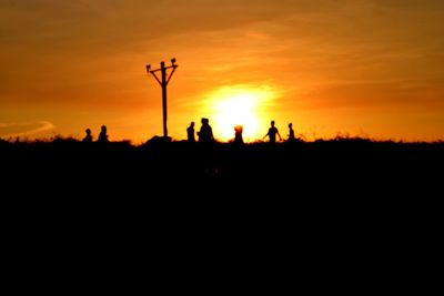 Silhouette people on field against orange sky