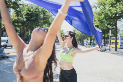 Fashionable young women holding blue textile in city during sunny day