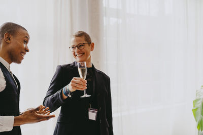 Smiling businesswoman holding drink glass while looking at male colleague during event at convention center