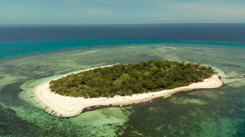 Tropical island and sandy beach surrounded by atoll coral reef and blue sea.  mantigue 