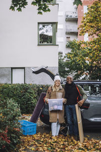 Portrait of smiling mature couple standing near car holding luggage