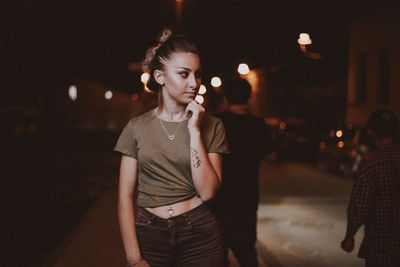 Thoughtful young woman looking away while standing on footpath at night