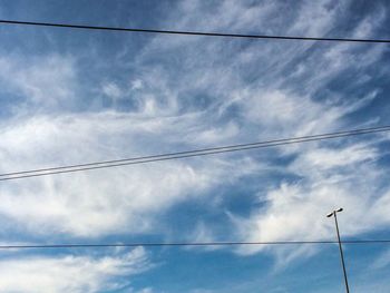 Low angle view of electricity pylon against cloudy sky