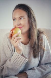 Portrait of young woman holding fruit against wall