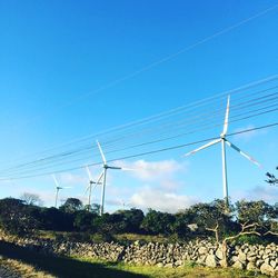 Low angle view of wind turbines on field against clear blue sky