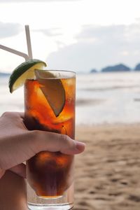 Close-up of hand holding drink at beach